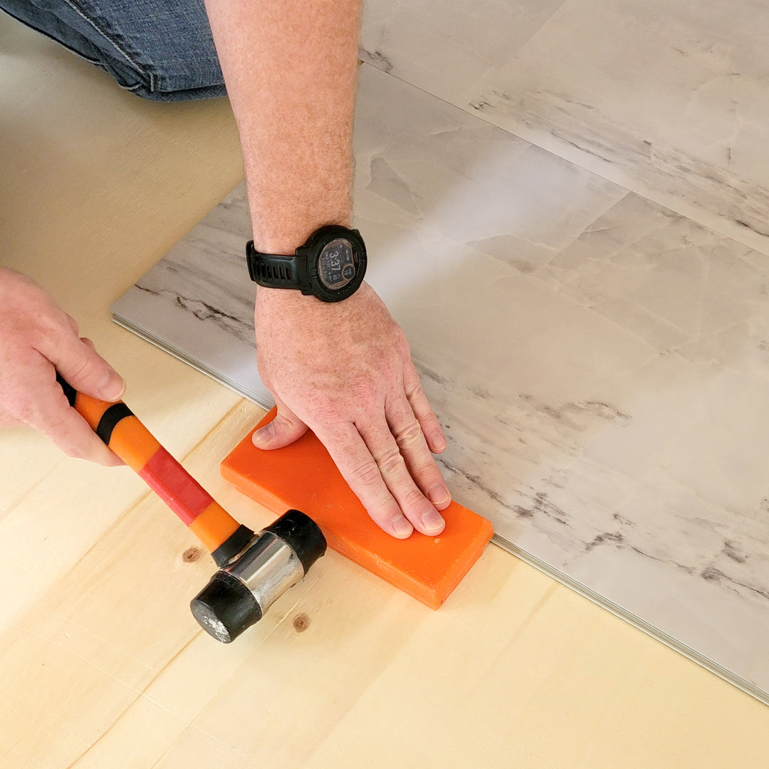 A person tapping in a piece of vinyl tile with a mallet