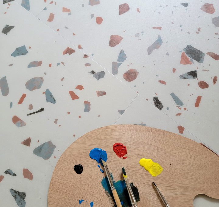 close up of Earl Grey terrazzo vinyl tiles with artists pallet, brushes, and paint